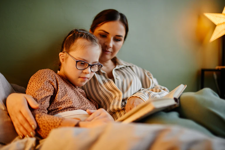 Photo d’une mère qui lit un livre avec sa fille atteinte de trisomie 21.