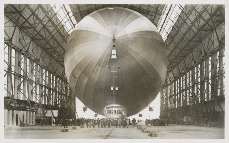 The giant airship in a hangar with people standing beside it looking very tiny