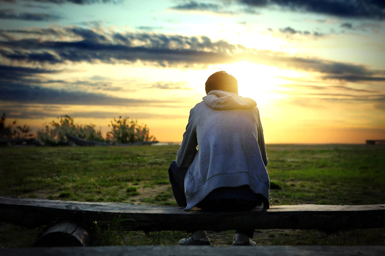 Boy looking out onto field of grass sunset