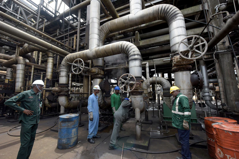 Men in overalls repairing the piping at an oil refinery.