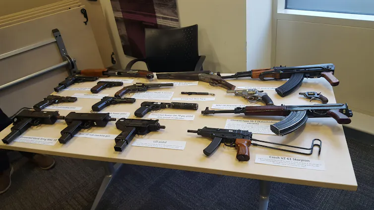 A number of labelled guns on a white table in an office room.