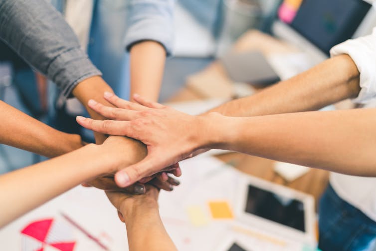 A group of team members placing their hands together in the centre of a circle