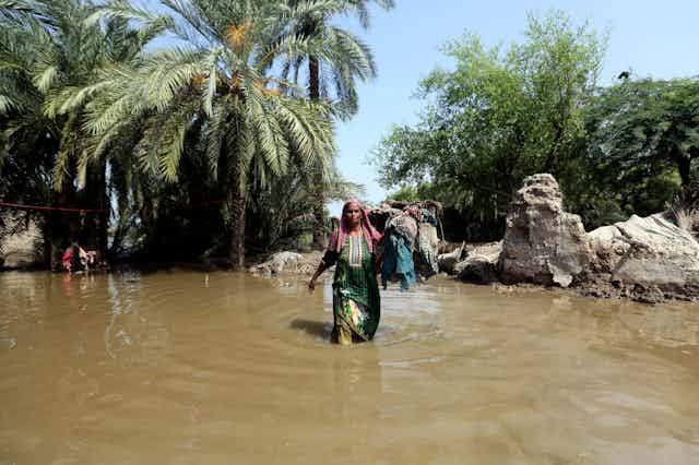 a woman wades through knee-high water carrying clothing in one hand