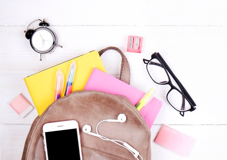 A backpack seen with notebook, glasses, a clock.