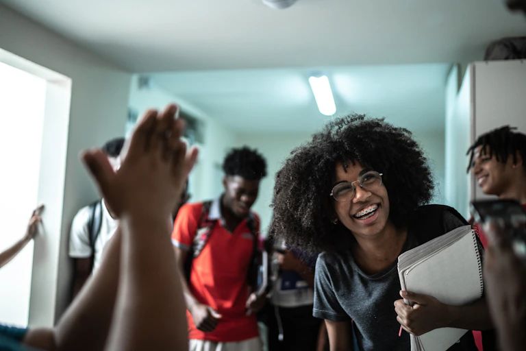 Five teenage students of color happily relaxing in school hallway.
