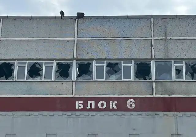 The grey facade of a building shows a line of broken windows.