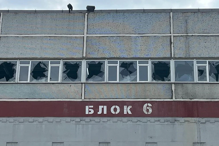 The grey facade of a building shows a line of broken windows.