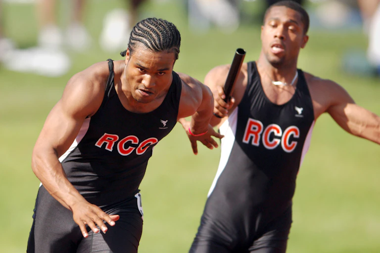 One runner from a community college track and field team hands a baton to another runner.