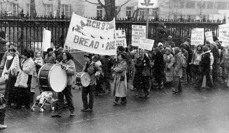 A black and white photo of a crowd of people marching down a street while holding protest signs