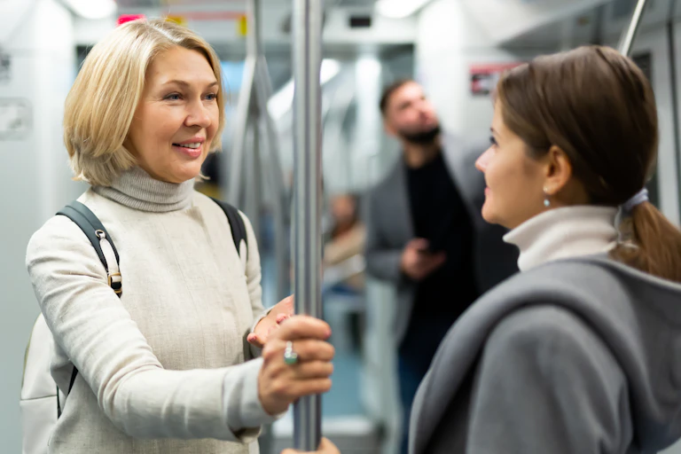 two women standing on a subway car smiling at each other
