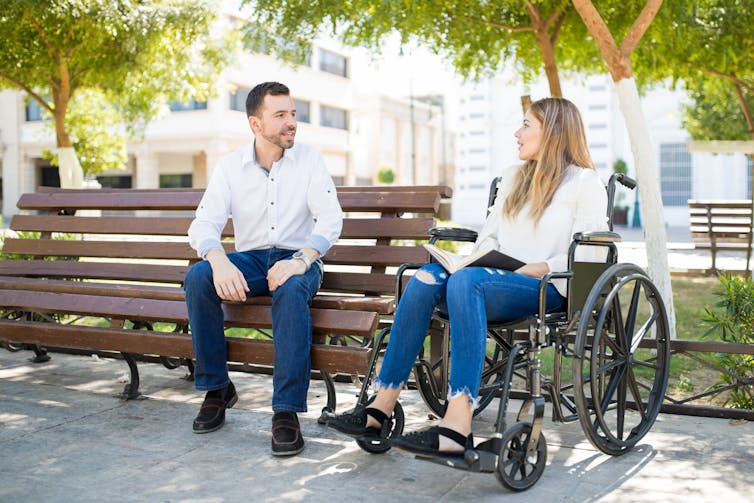 man sitting on park bench and woman in wheelchair talking