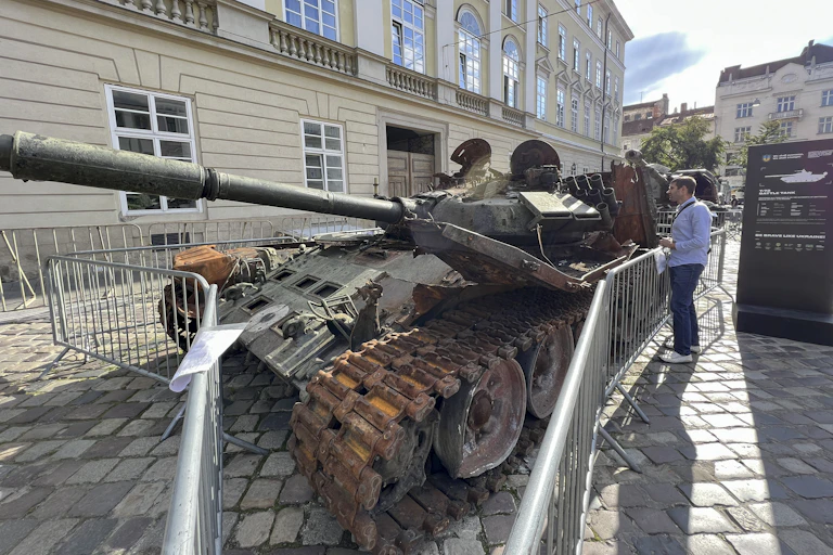 A man stands next to a wrecked, rusted tank