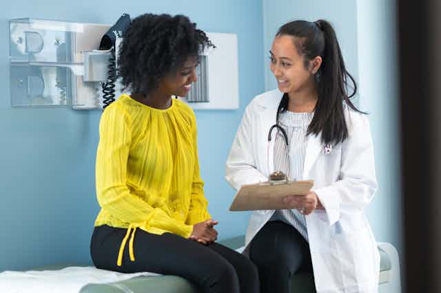 Doctor holding clipboard talking to patient sitting on exam table