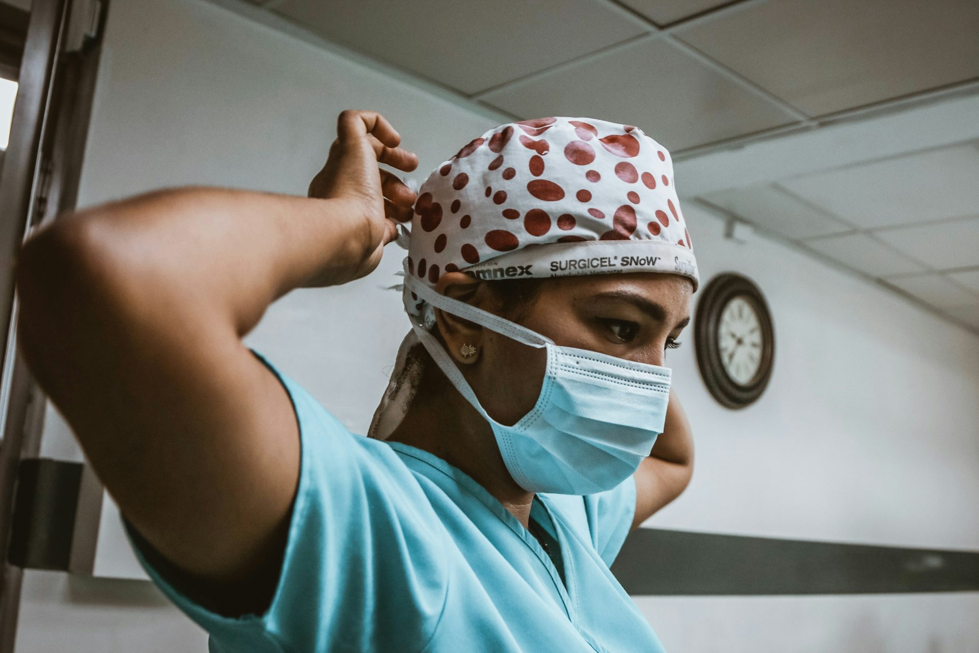 A non-white medical professional securing their mask and hair covering