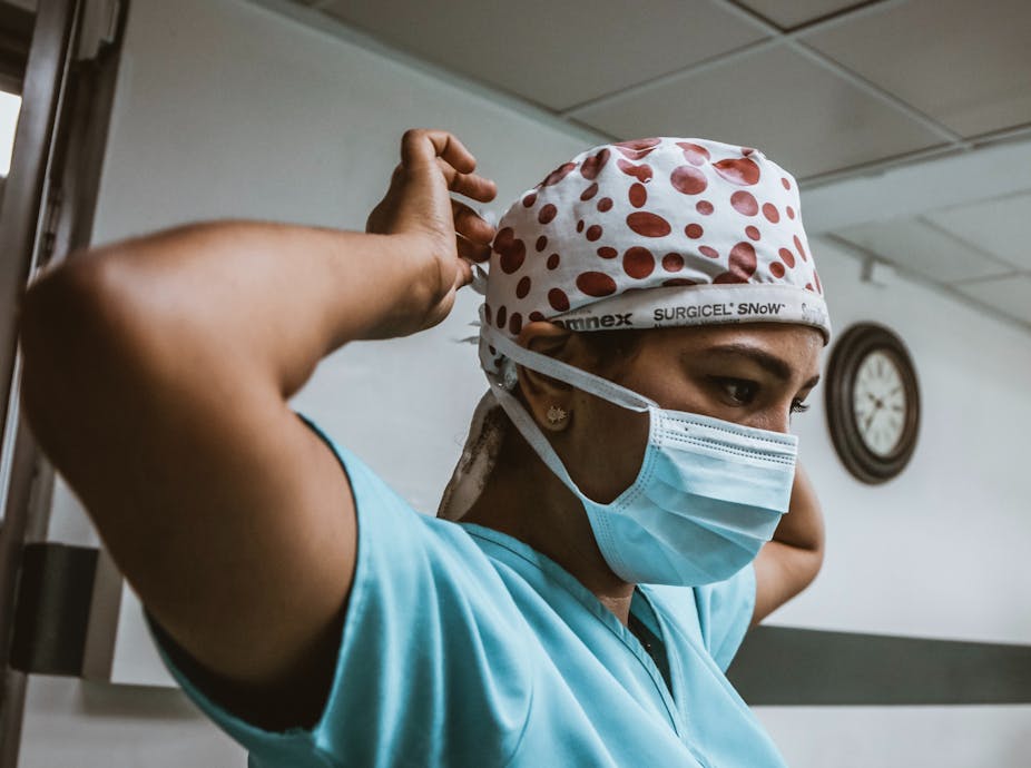 Woman in blue scrubs ties a surgical cap. 