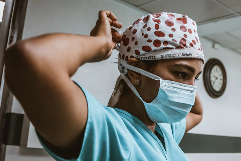 Woman in blue scrubs ties a surgical cap.