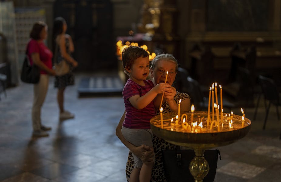 An elderly woman helps a child light candles in a church.