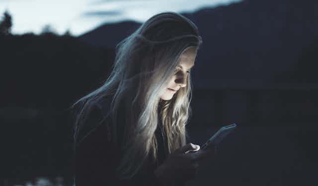 A woman outdoors transfixed on her phone late at night