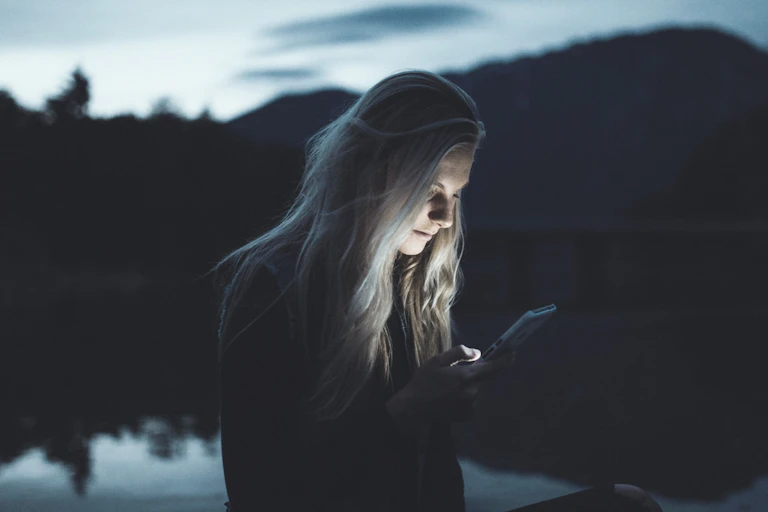 A woman outdoors transfixed on her phone late at night