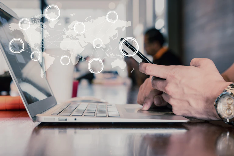 Person's hands with smartphone and laptop with global map overlaid