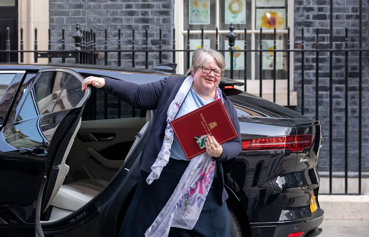 A smiling Therese Coffey steps out of a black car in front of Downing Street, holding a red minister's folder in front of her