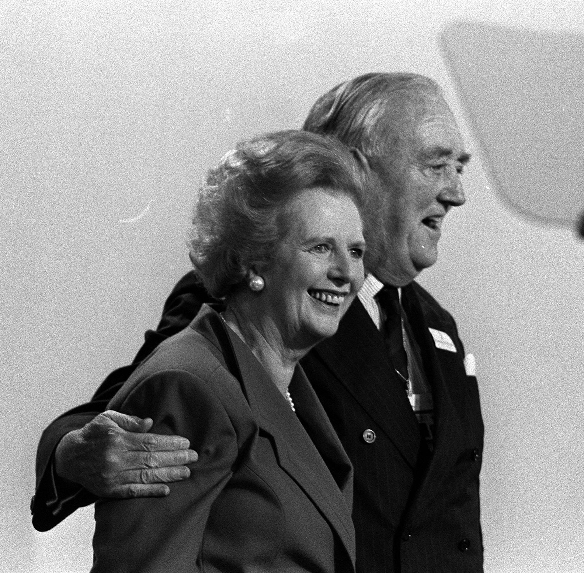 Black and white archive photo of Willie Whitelaw with his arm around Margaret Thatcher, both smiling and walking
