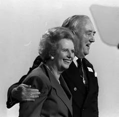 Black and white archive photo of Willie Whitelaw with his arm around Margaret Thatcher, both smiling and walking
