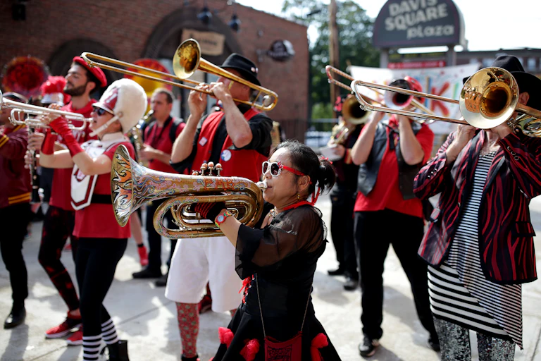 Musicians in unmatched red, white and black outfits march playing brass instruments.
