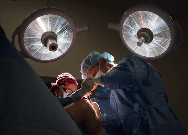 Deux personnes revêtues de sarrau en train de faire une opération au genou