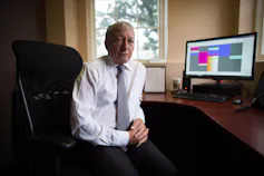 Un homme en cravate est assis, avec un ordinateur sur un bureau