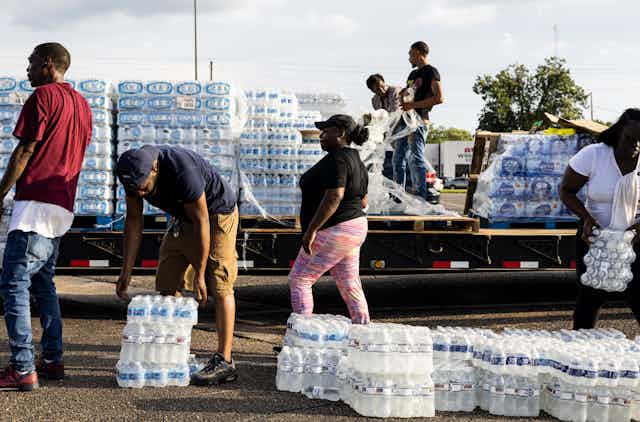 People pick up flats of bottled water from a truck