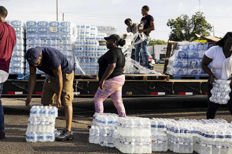 People pick up flats of bottled water from a truck