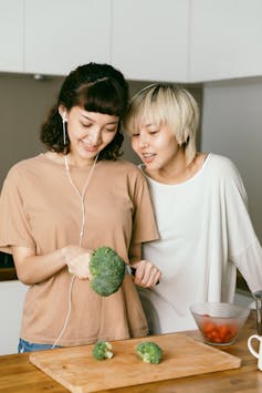 Two young people in front of a cutting board in a kitchen, with one holding broccoli