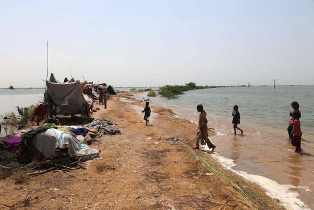 People and makeshift tents on a patch of land near floodwaters