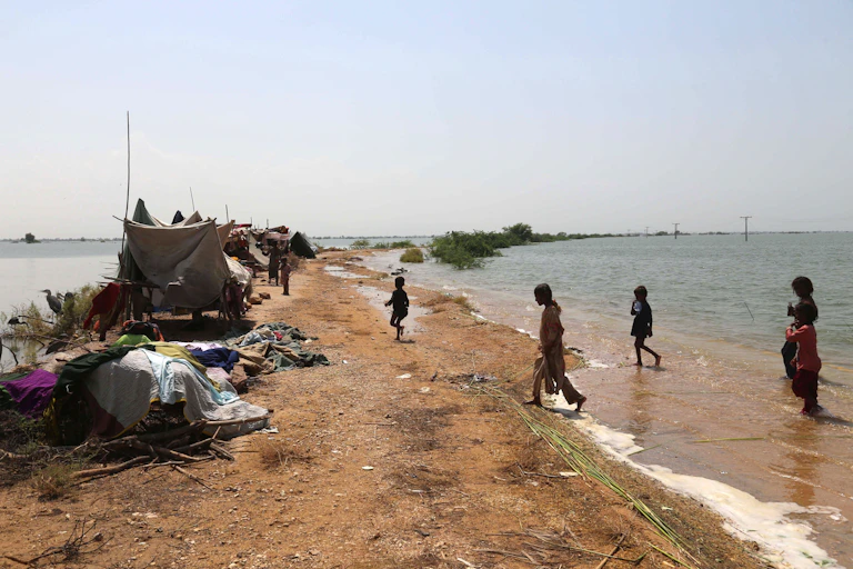 People and makeshift tents on a patch of land near floodwaters