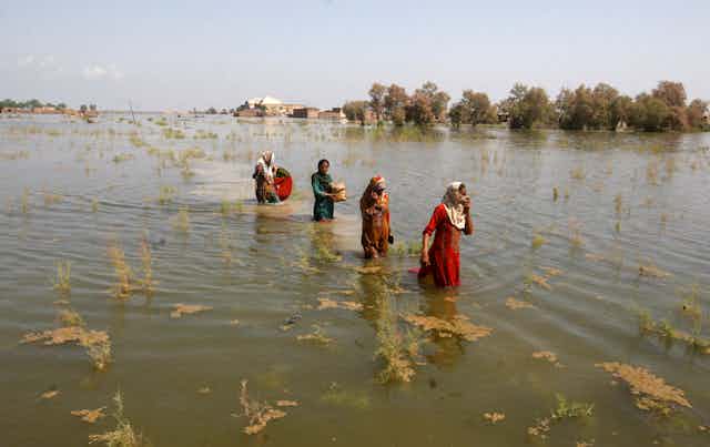 four women wade through a flooded plain