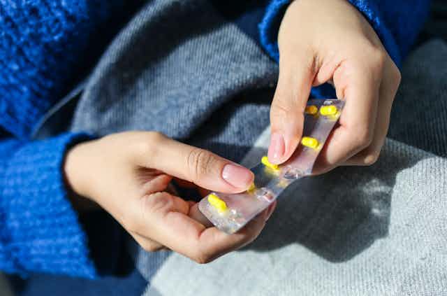 Person holding blister pack of medicine about to pop out yellow capsule
