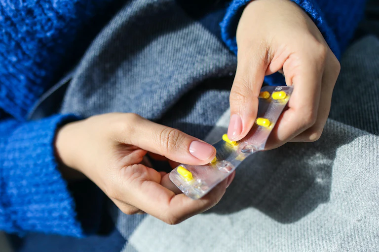 Person holding blister pack of medicine about to pop out yellow capsule