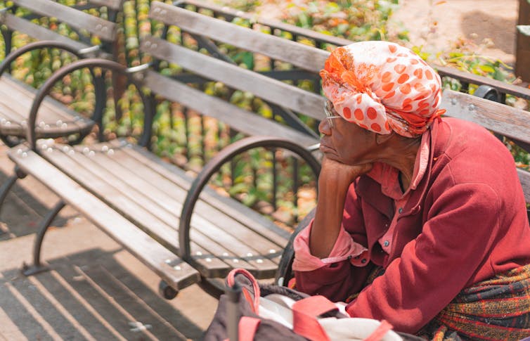 Older woman sits on a park bench, her head in her hand, resting