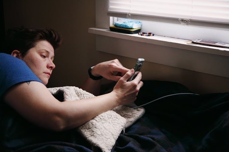 Person looks at their phone while laying in bed, by a window