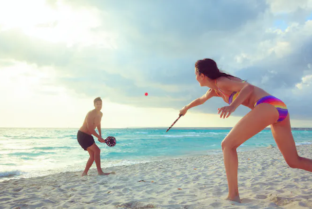 Pemandangan pantai yang damai dengan pasangan muda yang bugar bermain tenis pantai