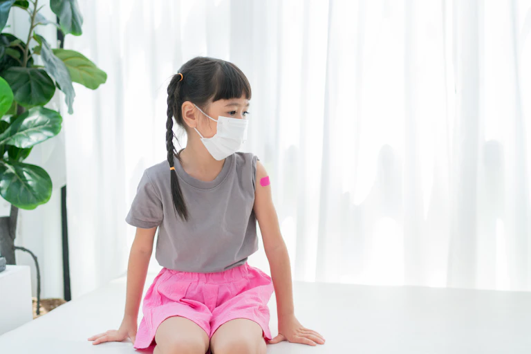 A girl with a mask on and a plaster on her upper arm.