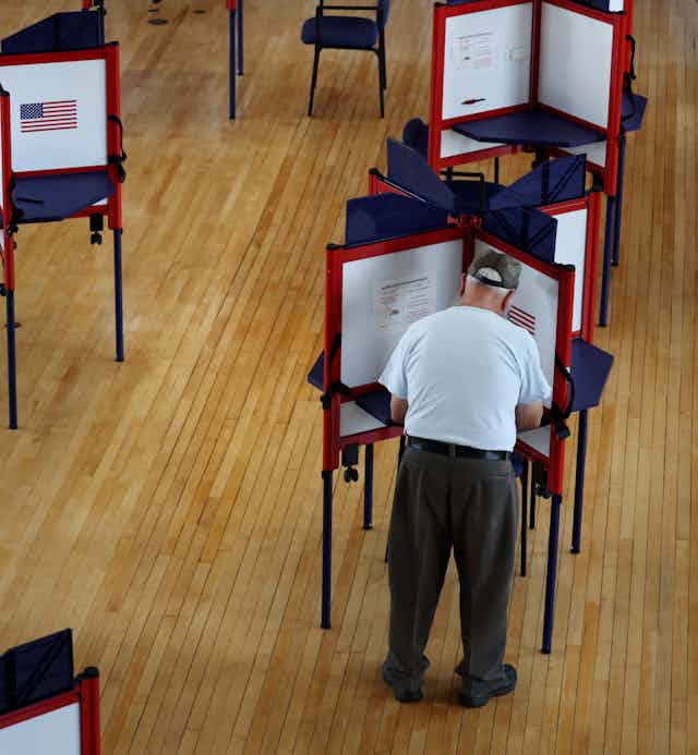 A man is filling out his ballot at one of several voting booths. 