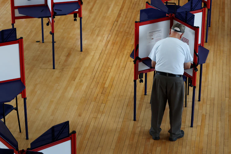 A man is filling out his ballot at one of several voting booths.