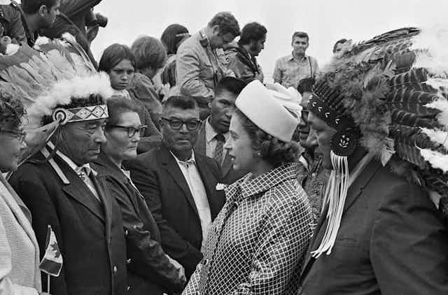 The Queen meets with a group of Indigenous people, some of whom are wearing traditional headdresses.