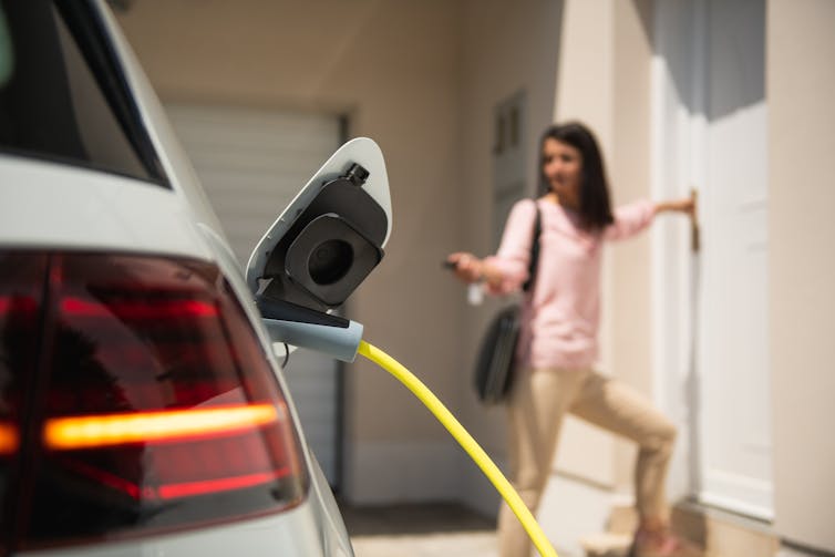 A woman locks her car, which is plugged in and charging.