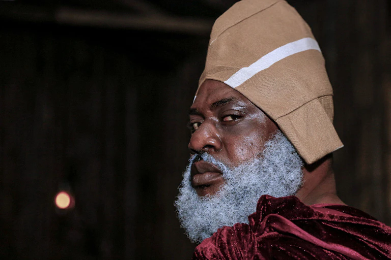 A man with a greying beard looks into the camera over his shoulder, a fierce expression on his face.