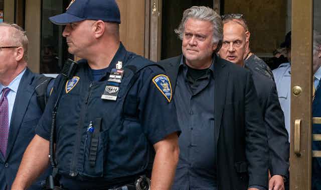 Steve Bannon surrounded by a police officer and men in suits