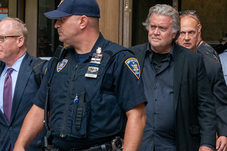 Steve Bannon surrounded by a police officer and men in suits