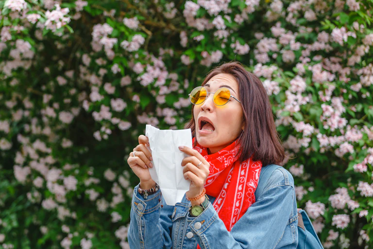 A person is outside sneezing into a tissue.